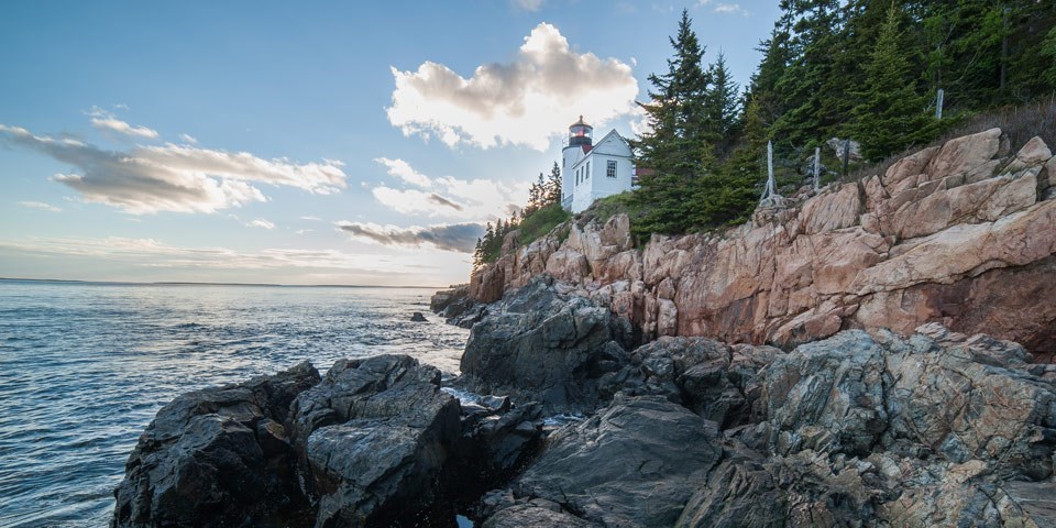 Lighthouse on the side of a cliff at Bass Harbor, with near cloudless blue skies and calm ocean