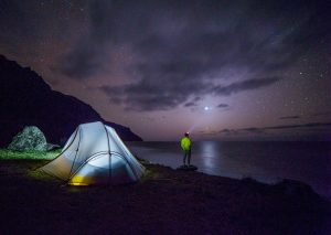 Camper under the night sky with tent. The best camping gear means you can camp anywhere.
