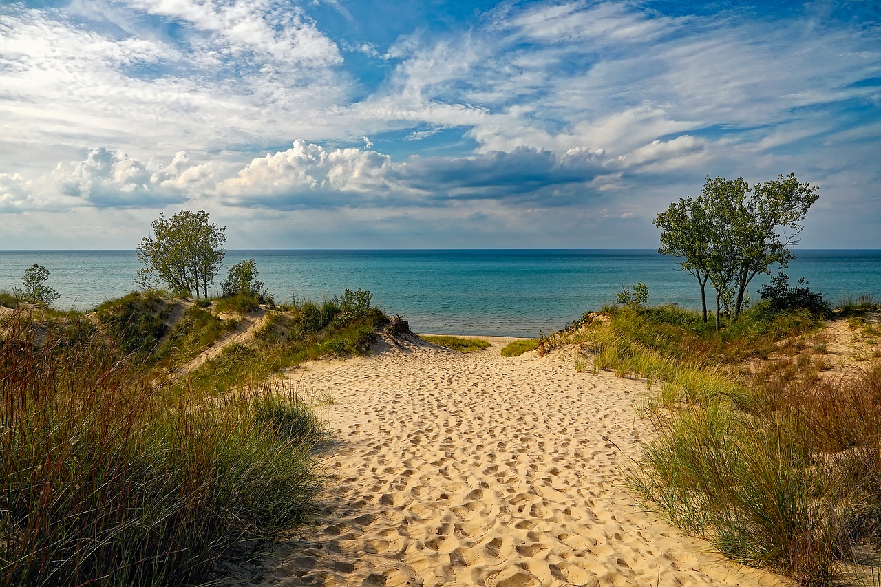 Looking across sand dunes to the azure waters and blue sky with fluffy white clouds at Indiana Dunes State Park Beach.